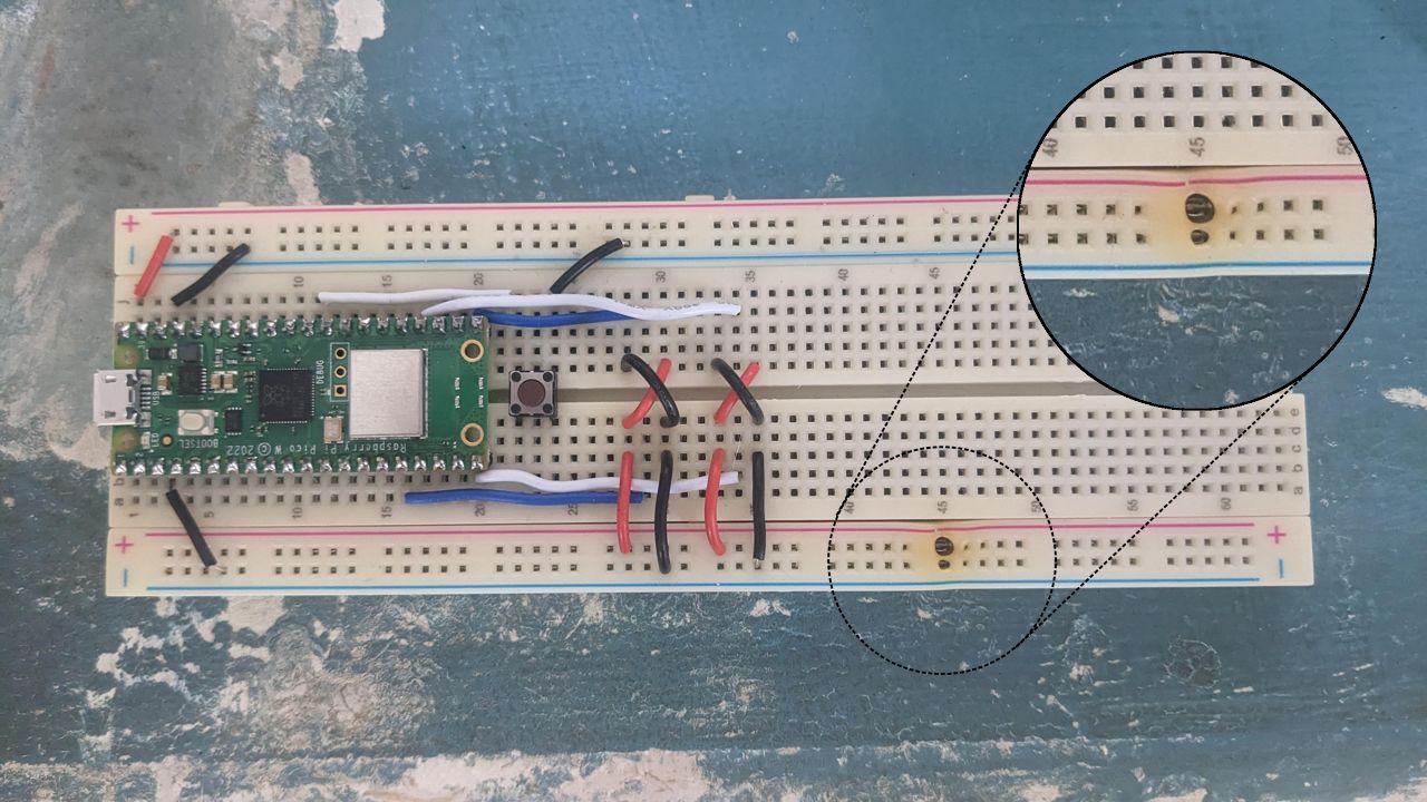 A picture of the breadboard containing the Pico W and various linking various rows. Notably, one hole of the bottom positive rail is discoloured and clearly partially melted.